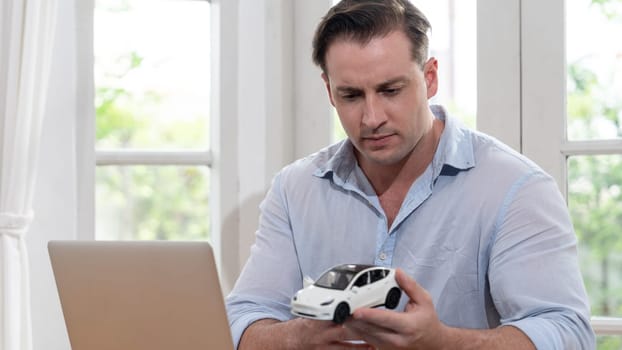 Car design engineer analyze car model prototype for automotive business company at home office. Vehicle designer holding scale car, carefully analyzing looking for any flaw or improvement. Synchronos