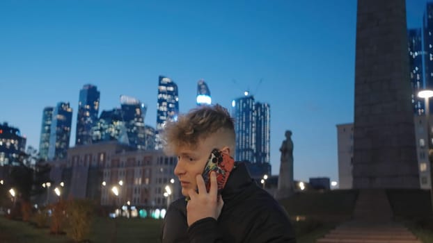 Young man is talking on phone on background of modern city. Action. Man is talking on phone while walking around city.