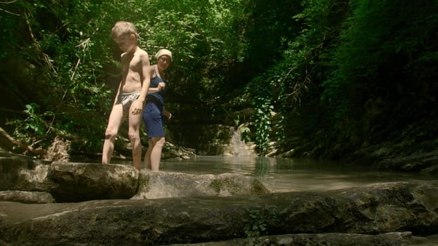 Boy kid and his mother having a great time in the cold mountain stream. Creative. Beautiful river and jungles