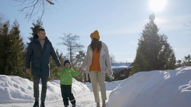 Young family in a city winter park. Action. Man, woman, and their child having fun and walking near trees and snow