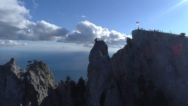 Gorgeous scenery from above. Aerial view of high white cliff and and people with flags on the top against the sea and small city on the shore in summer day