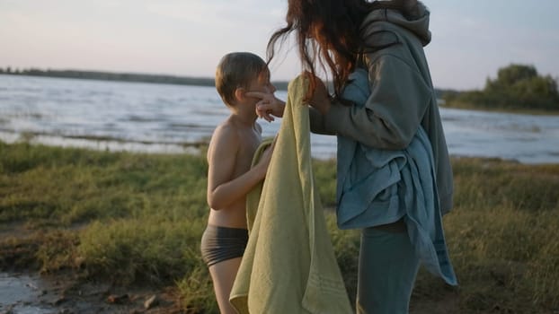 Mother wipes son after swimming on beach. Creative. Mother and son after swimming in village lake in evening. Relaxing on village lake and swimming in evening.