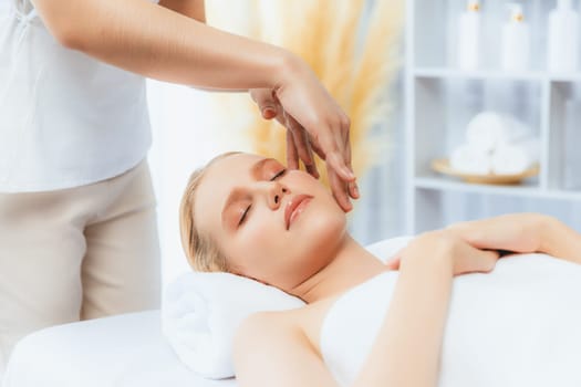 Caucasian woman enjoying relaxing anti-stress head massage and pampering facial beauty skin recreation leisure in dayspa modern light ambient at luxury resort or hotel spa salon. Quiescent