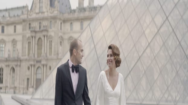 Walking bride and groom with a glass facade Louvre pyramid. Action. Loving beautiful man in woman on their wedding day