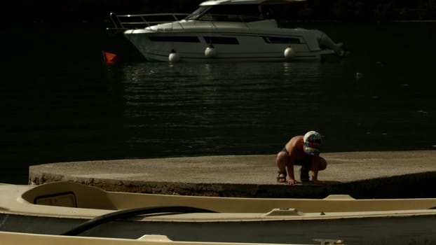 Boy walking on wooden pier along the yachts. Creative. Little boy spending time near the lake