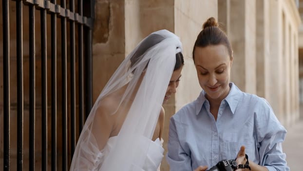 Photographer showing pictures to a model young bride. Action. Wedding photosession outdoors