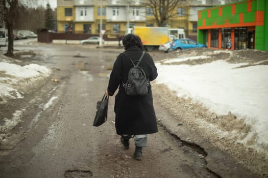 Woman walks along dirt road in city. Man in black jacket with backpack. Woman in Eastern Europe.