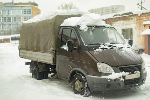 Freight transport in snow. Russian truck. Gray body of machine. Industrial zone in winter.