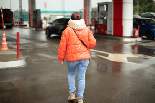 Girl goes to gas station with gasoline. Woman in parking lot. Man on street. Petrol station in city.