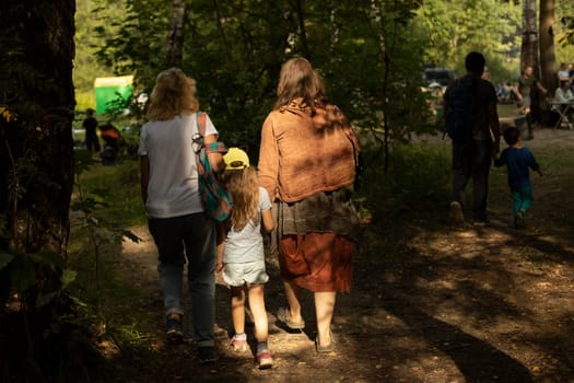 Family with child at festival in summer. Parents with child in park. Rest and travel. People from behind in sunlight.