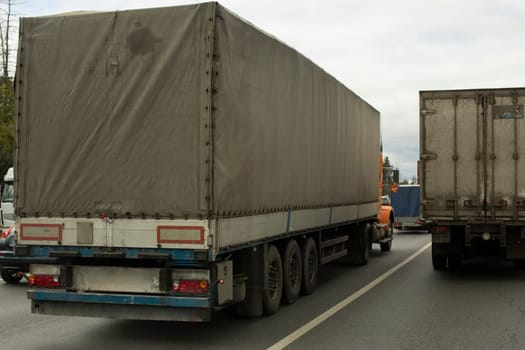 Truck is driving down highway. Large trailer on track. Transportation of goods in summer. Awning on body. Large load on highway.