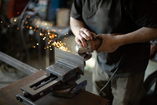 Guy in garage is repairing steel part. Man grinds iron. Person fixes steel blank.