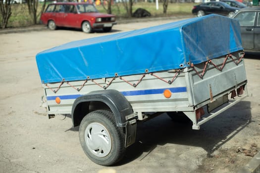 Trailer for car. Blue awning on trailer body. Transport in parking lot. Two-wheeled vehicles.