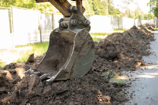 Escalator bucket digs ground. Heavy machinery at construction site. Laying pipes in ground. Steel bucket for raising ground.