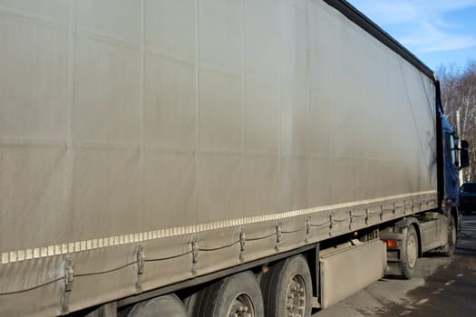 Truck with trailer. Grey awning on truck body. Transport side view. Car on road. Transportation of goods.