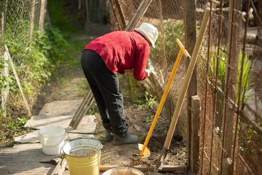 Pensioner in garden in summer. Grandma works in garden. Elderly person on vacation. Repair of fence on your own.