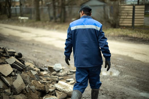 Worker in blue clothes. Road worker removes rocks. Man on construction site.