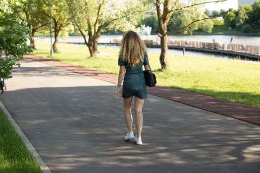 Girl walks through park in summer. Walk in summer on street. Shooting woman from back. Resident of city walks along road.