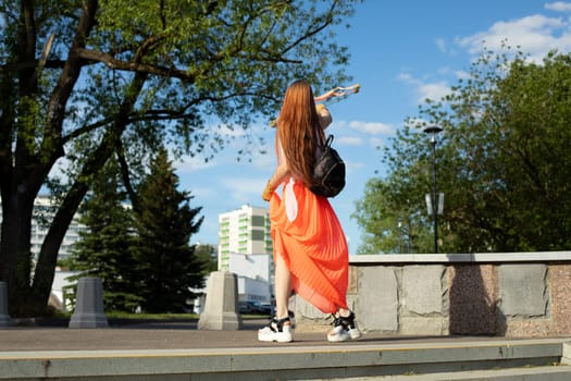 Girl in orange dress in city. Beautiful clothes. Bright clothes of girl. Student walking in park.