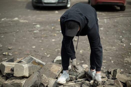 Guy picks up rock Man in black jacket. Unknown person is looking for cobblestone.