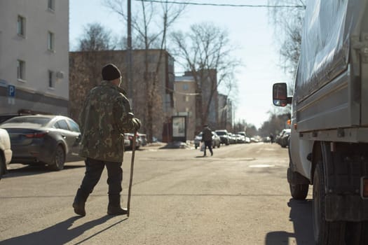 Grandpa walks through square. Elderly man in town. Man with stick. Pensioner on street. Walking alone.