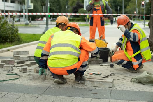 Workers make road. Repair of pedestrian zone. Three workers in helmets are sitting.