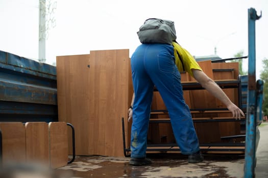 Loader loads furniture into back of truck. Transportation of furniture. Person puts tables in car. Man in blue pants.