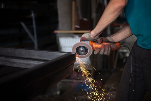 Metal processing. Grinder in hand. Worker holds tool. Creation of steel structure. Work in garage.