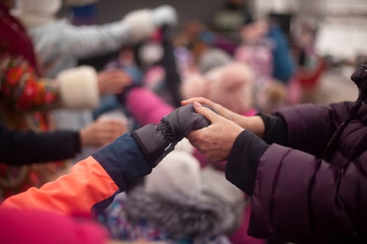 People holding hands while playing outside. Baby and ingrown hands. Team play in detail. Hand in children's glove in winter.