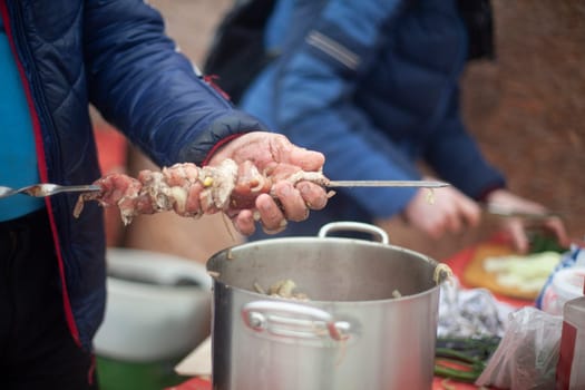 Putting meat on knife. Cooking meat with your hands. Street food. Folk Caucasian cuisine. Man holding piece of meat and skewer.