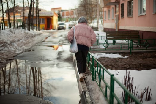 Girl walks down street in winter. Woman in winter in city. Bad road in yard in Russia. Student returns home.