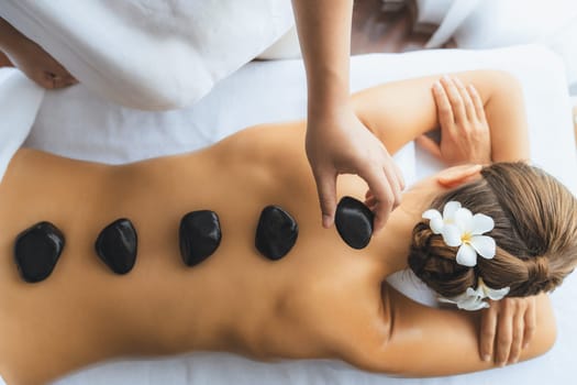 Panorama top view hot stone massage at spa salon in luxury resort with day light serenity ambient, blissful woman customer enjoying spa basalt stone massage glide over body. Quiescent