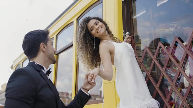 Romantic date outdoors in the city street. Action. Woman on the stairs of the tram car with her hand in a hand of a man in black suit