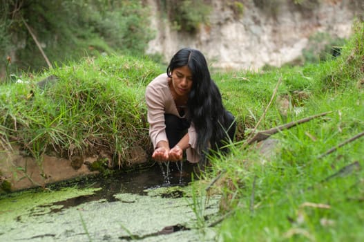 latin american girl next to a lagoon catching water with both hands surrounded by nature.earth day. High quality photo