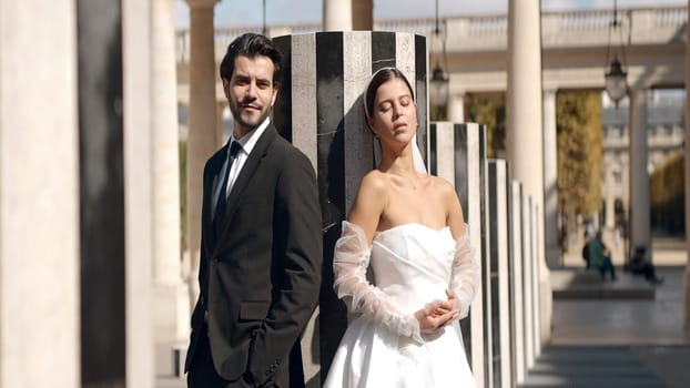 Beautiful couple of newlyweds at photo shoot on sunny day. Action. Attractive couple of newlyweds posing on background of old architecture. Couple of newlyweds with sunny summer day.