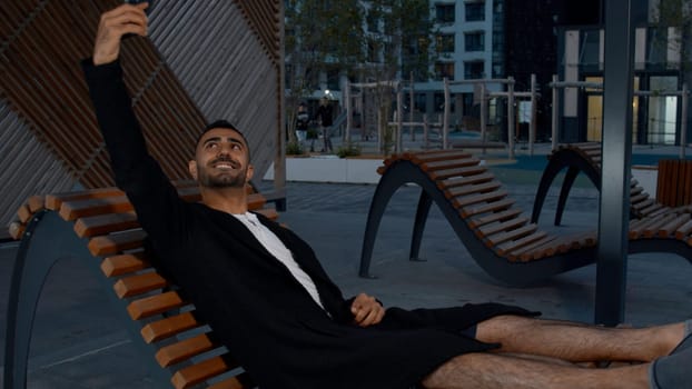 A handsome well-groomed man in summer clothes. Media. Summer pastime on a bench in the park and talking on the phone smiling at the camera. High quality 4k footage