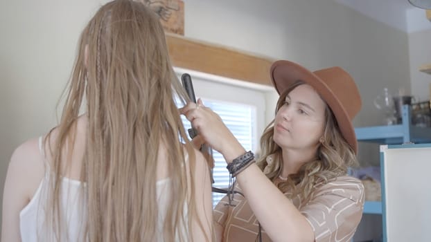 Female stylist does model's hairstyle. Action. Cute hairdresser does woman's hairstyle for photo shoot. Woman twists model's hair for photo shoot.