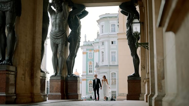 A young couple walking. Action . Beautiful newlyweds with a bride in a lush long white dress and with their groom walking down the street next to the monuments on the square. High quality 4k footage