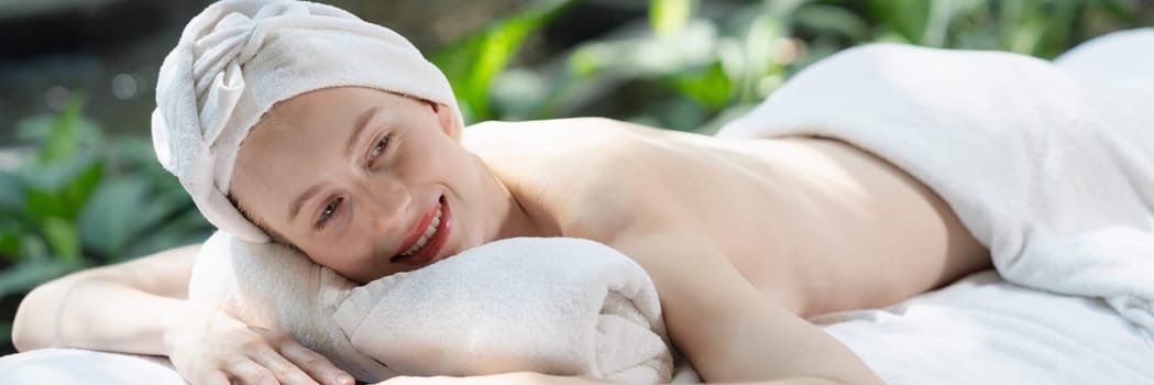 Beautiful young woman relaxes on a spa bed surrounded by nature. ready for a body massage. Attractive female in white towel lying peacefully during waiting for body massage. Close up. Tranquility