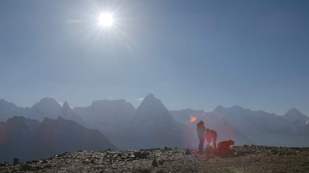 Tourists on background of mountain landscape with bright sun. Creative. Beautiful motivating view of peaks of snowy mountains in rays of sun. Hikers on background of mountain peaks on sunny day.