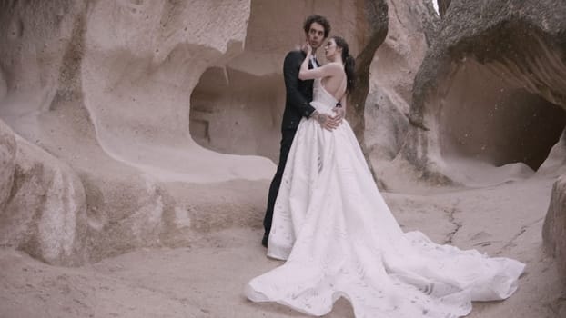 Beautiful bride and groom on background of rocks. Action. Newlyweds pose in natural landscape of rocks. Newlyweds embrace at rocky wall.