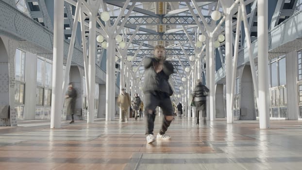 Young man dancing in city. Action. Modern dancer moves in crowd of people. Young man dances with people passing by.