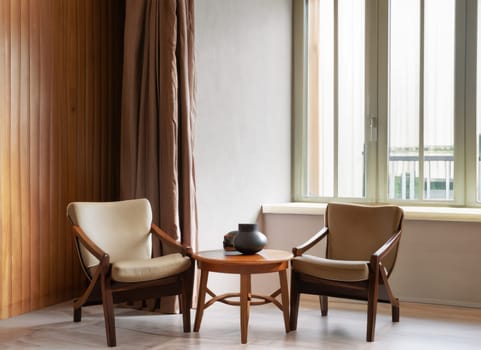  Two barrel chairs and round wooden coffee table against window near paneling wall