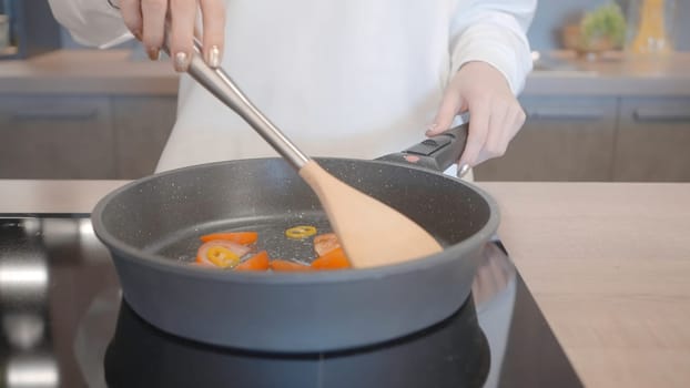 Close-up of woman cooking in new frying pan. Action. Roasting vegetables on new modern model of frying pan. Cooking healthy food in new frying pan.