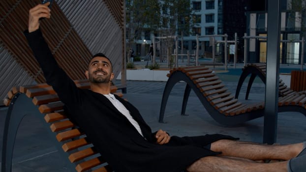 A bench with a man lying resting. Media. An evening park with a calm atmosphere where a young man is resting lying down. High quality 4k footage