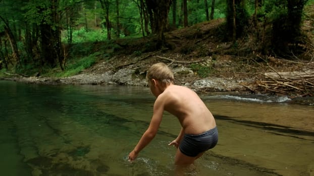 Reaction of a little boy on cold water in forest. Creative. Stream with clear water and dense forest