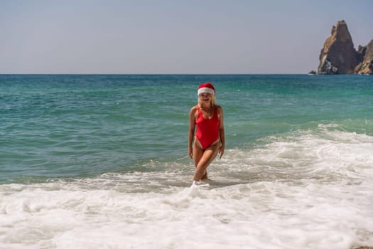 A woman in Santa hat on the seashore, dressed in a red swimsuit. New Year's celebration in a hot country.