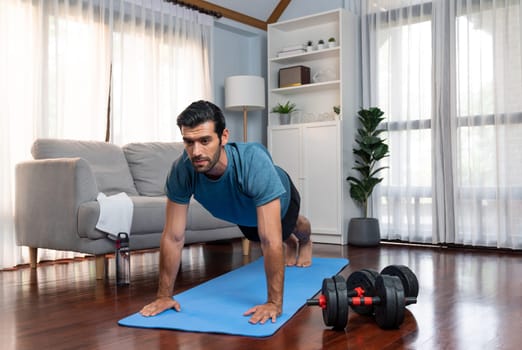 Athletic and sporty man doing pushup on fitness mat during home body workout exercise session for fit physique and healthy sport lifestyle at home. Gaiety home exercise workout training.