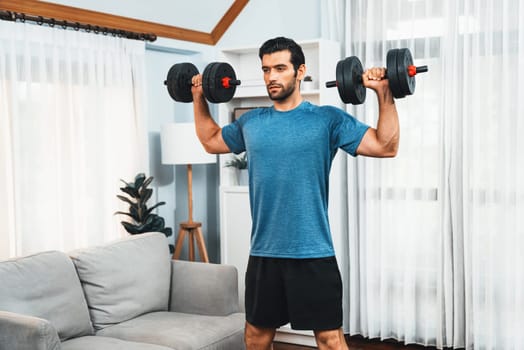 Athletic body and active sporty man lifting dumbbell weight for effective targeting muscle gain at gaiety home as concept of healthy fit body home workout lifestyle.