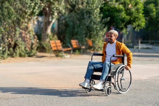 Young African American man sitting on a wheelchair outdoors in park. Copy space.